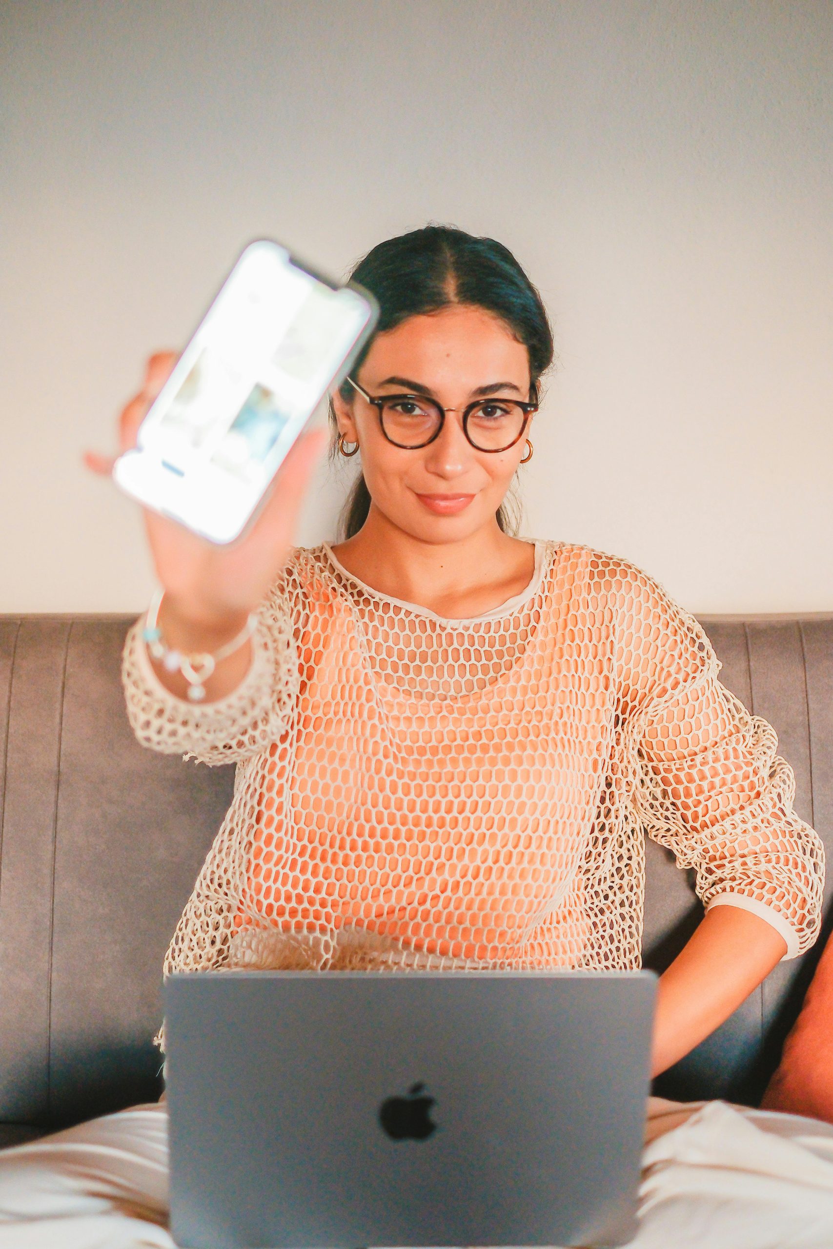 A confident young woman uses a laptop and smartphone on a sofa, symbolizing modern technology and connectivity.