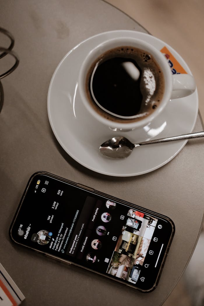 A cup of black coffee next to a smartphone displaying a social media app on a cafe table.