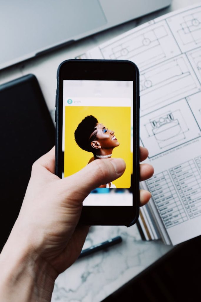 A smartphone displaying a vibrant portrait held over technical drawings on a desk.