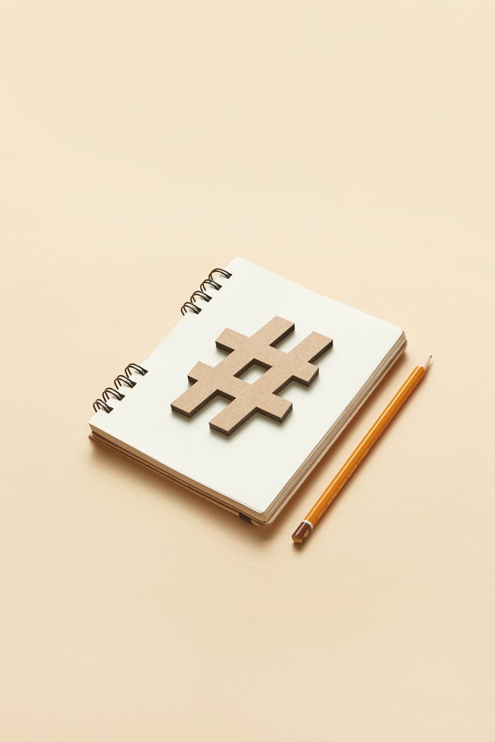 A minimalist setup with a notebook, wooden hashtag symbol, and pencil on a beige background.